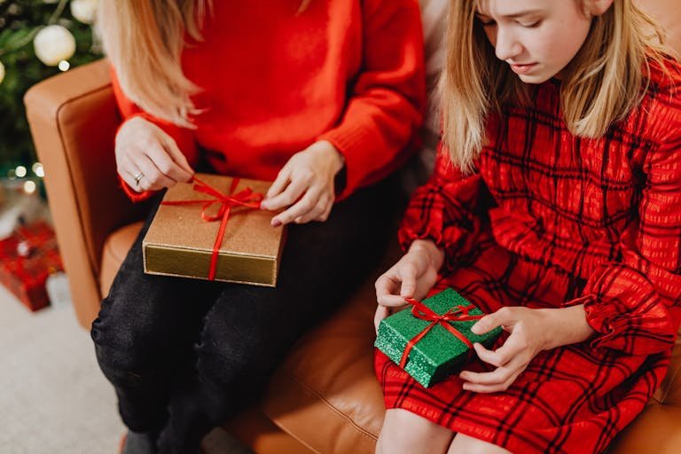 Mother and daughter sitting on a sofa, opening Christmas presents in a cozy living room.